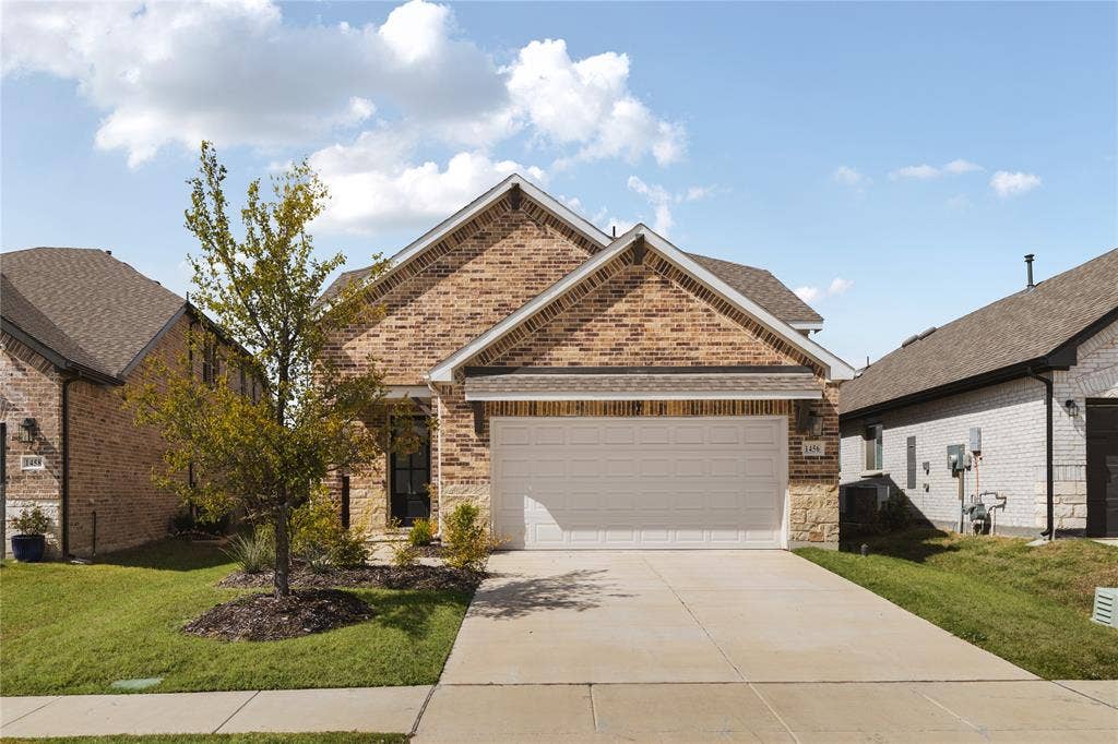 1456 Martingale Lane, Forney, TX 75126 Brick and stone exterior featuring a double-gabled roofline, front-facing two-car garage, and concrete driveway