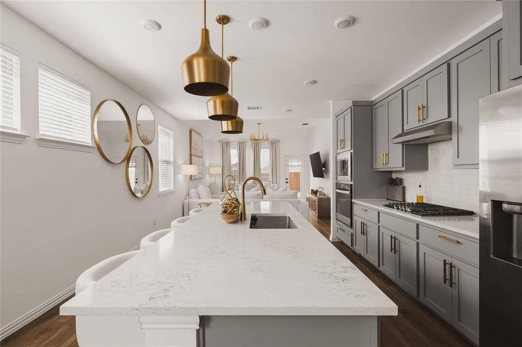 1456 Martingale Lane, Forney, TX 75126 Kitchen featuring a quartz-topped island with an undermount sink, grey cabinetry with brass-finish hardware, built-in stainless steel oven, gas cooktop, and brass pendant lighting