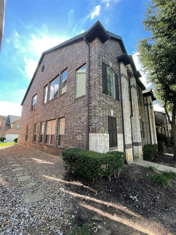 1944 Loma Linda Drive, Irving, TX 75063 Multi-story exterior featuring dark brick masonry, contrasting stone accents, multi-pane windows with dark shutters, and a gravel-based side landscape