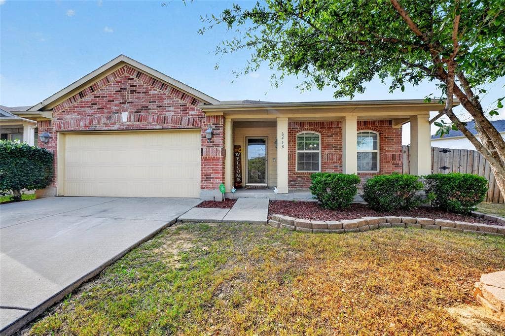 8448 Little Fawn Lane, Dallas, TX 75249 Single-story brick exterior featuring a covered front porch with support columns, an attached two-car garage, and a stacked stone garden border