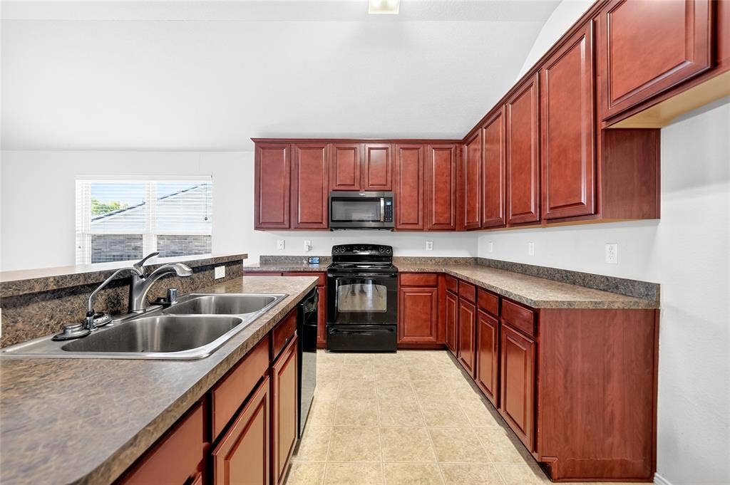 8448 Little Fawn Lane, Dallas, TX 75249 Kitchen featuring cherry-finish cabinetry, solid-surface countertops, dual-basin stainless steel sink, black appliances, and neutral-tone floor tiling