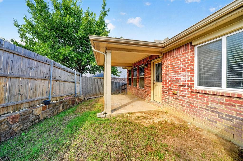 8448 Little Fawn Lane, Dallas, TX 75249 Covered concrete patio with a brick exterior, stone retaining wall, and wood-finish perimeter fencing