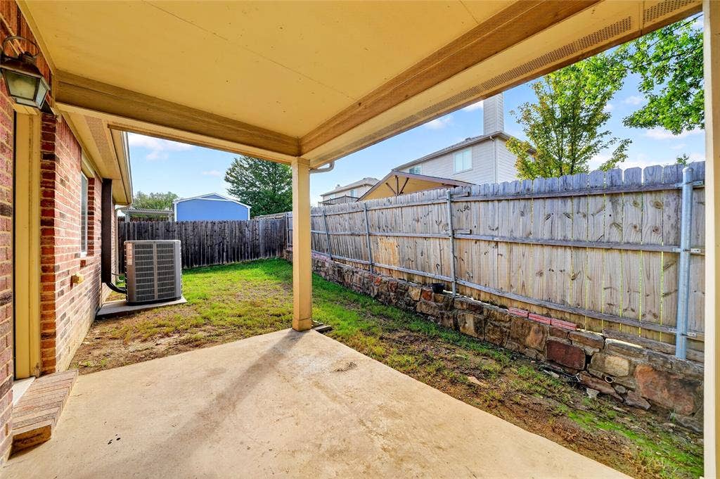 8448 Little Fawn Lane, Dallas, TX 75249 Covered concrete patio featuring brick exterior siding, a natural stone retaining wall, and a wood privacy fence