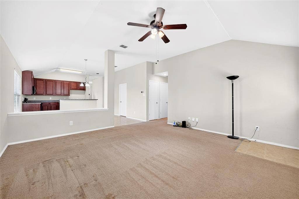 8448 Little Fawn Lane, Dallas, TX 75249 Open-concept interior featuring vaulted ceilings, a ceiling fan with integrated lighting, wall-to-wall carpeting, and wood cabinetry in the kitchen