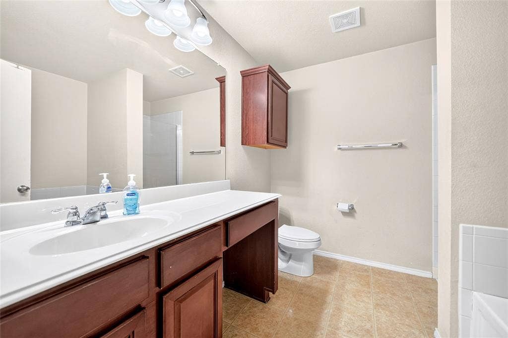 8448 Little Fawn Lane, Dallas, TX 75249 Bathroom vanity featuring a solid-surface countertop with an integrated basin, dark wood-finish cabinetry, a large wall-mounted mirror, and overhead tri-light fixture