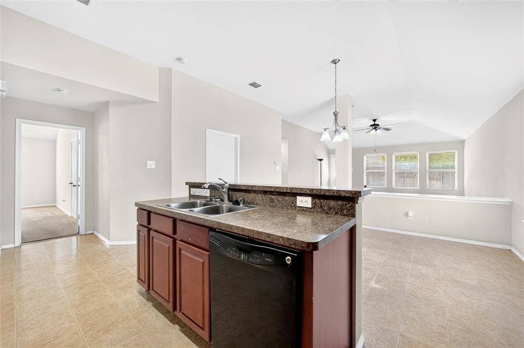 8448 Little Fawn Lane, Dallas, TX 75249 Kitchen featuring a raised breakfast bar, dark-toned cabinetry, dual-basin stainless steel sink with pull-down faucet, and neutral tile flooring