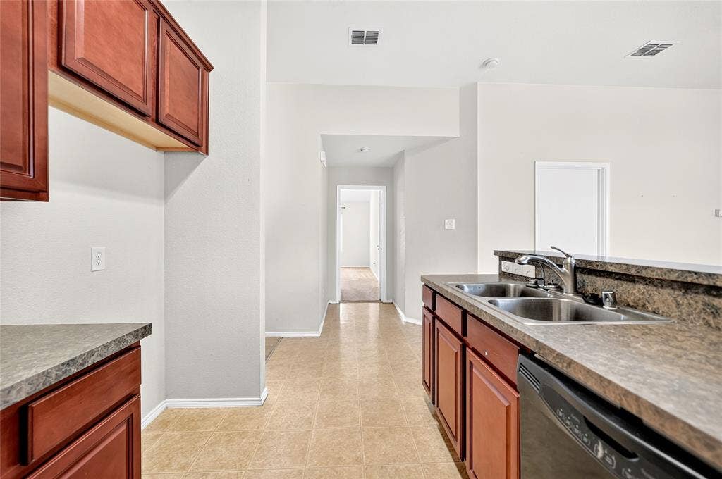 8448 Little Fawn Lane, Dallas, TX 75249 Kitchen area featuring wood-finish cabinetry, stone-texture laminate countertops, a double-basin stainless steel sink with a high-arch faucet, and tile flooring