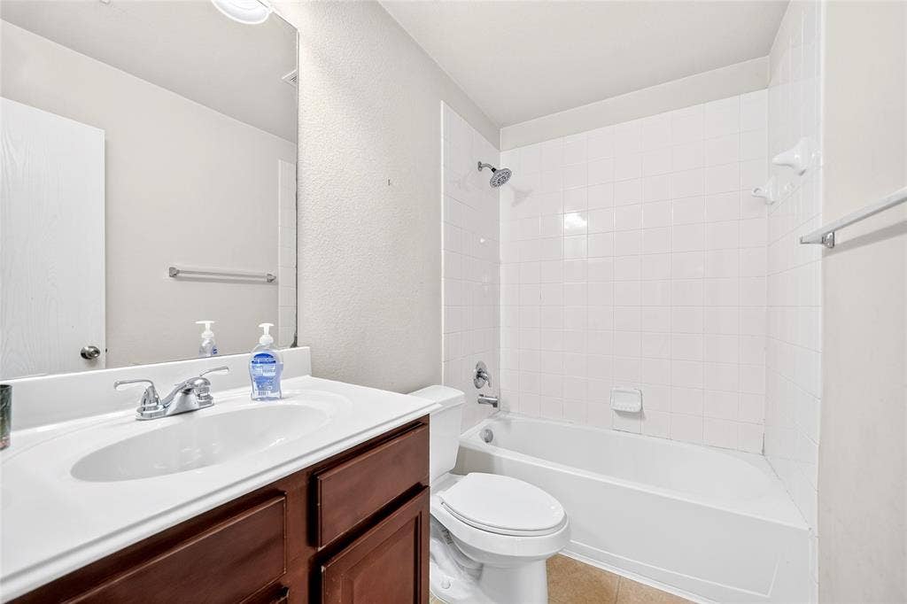 8448 Little Fawn Lane, Dallas, TX 75249 Bathroom featuring a wood-tone vanity, white countertop, integrated sink with a chrome faucet, and a tub-shower combination with white wall tile