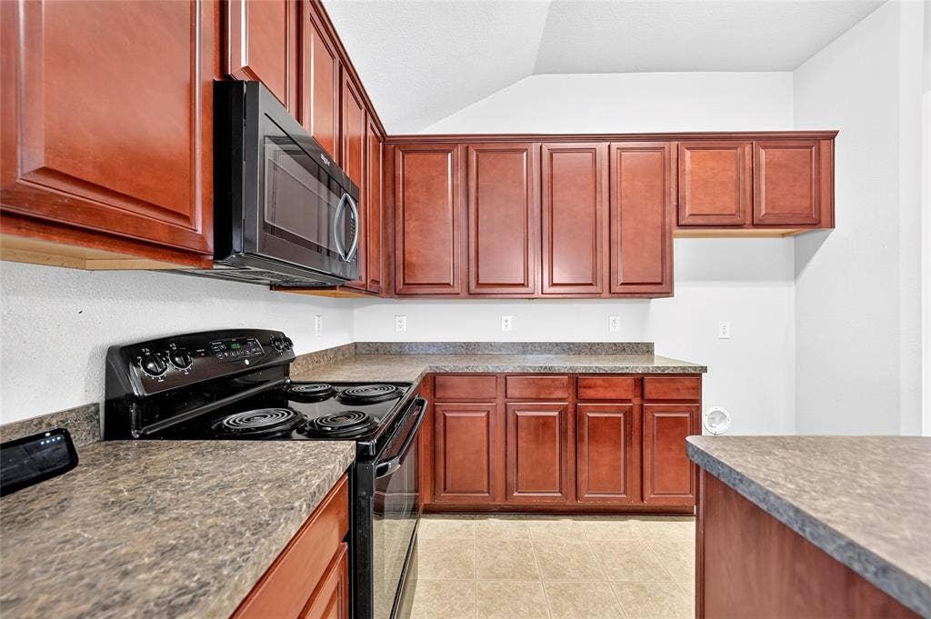 8448 Little Fawn Lane, Dallas, TX 75249 Kitchen featuring stained wood cabinetry, laminate countertops, a black electric range, and an over-the-range microwave