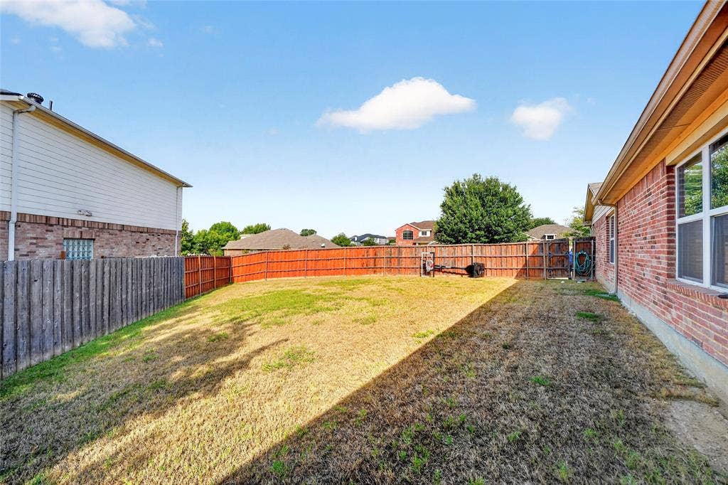 8448 Little Fawn Lane, Dallas, TX 75249 Rear exterior featuring red brick and light-toned siding, grass lawn, and perimeter wood privacy fencing
