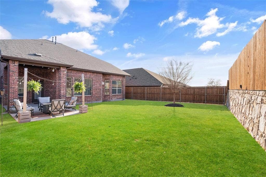 1017 Hoyt Drive, McKinney, TX 75071 Expansive backyard featuring a covered patio with brick columns, a stone and wood privacy fence, and a manicured lawn
