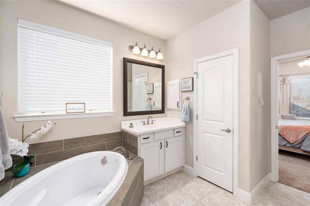 1017 Hoyt Drive, McKinney, TX 75071 Soaking tub with tile surround, single vanity with integrated sink, rectangular mirror, and sconce lighting