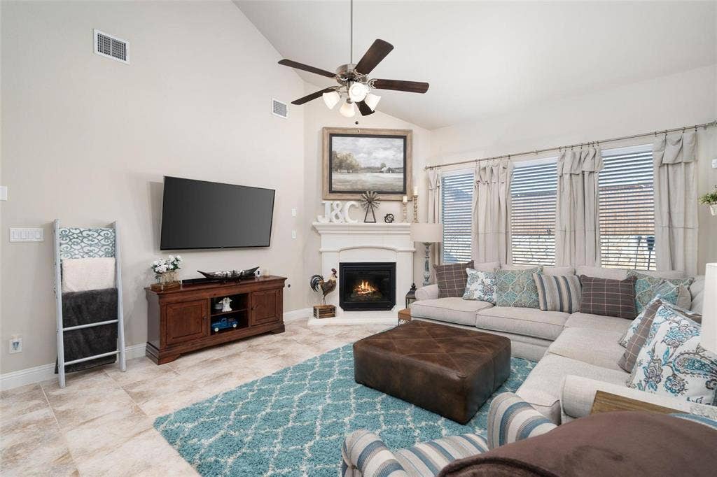 1017 Hoyt Drive, McKinney, TX 75071 Vaulted ceiling with a ceiling fan, corner fireplace with a mantel, multiple windows with blinds, and tile flooring