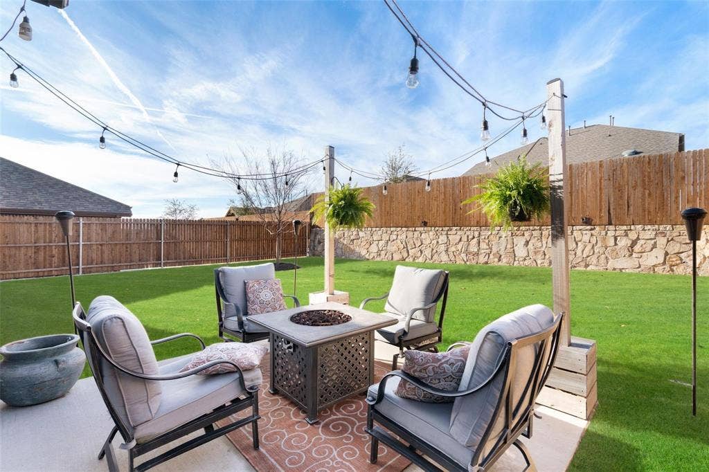 1017 Hoyt Drive, McKinney, TX 75071 Expansive backyard featuring a manicured lawn, wood privacy fencing, stone wall accent, string lighting, and a paved patio area