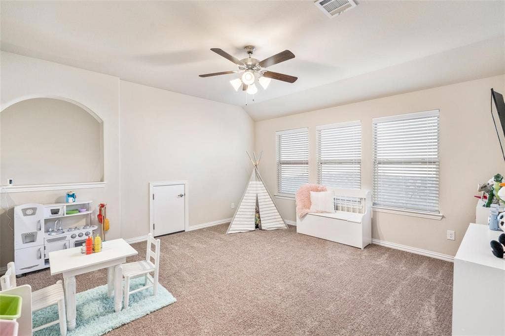 1017 Hoyt Drive, McKinney, TX 75071 Carpeted room with a ceiling fan, three windows with blinds, a white door, and an arched wall opening
