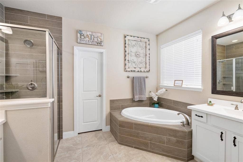 1017 Hoyt Drive, McKinney, TX 75071 Tiled walk-in shower with glass enclosure, separate soaking tub, single vanity with white cabinetry, and large framed mirror