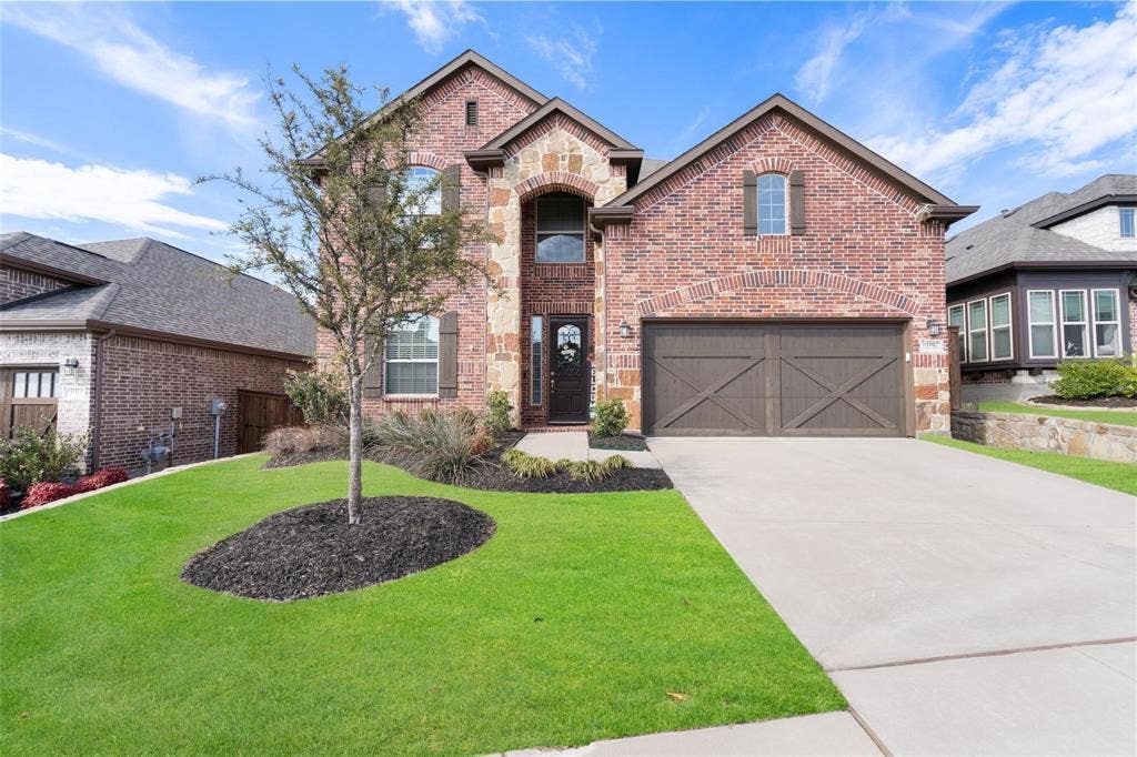 1017 Hoyt Drive, McKinney, TX 75071 Brick and stone facade, arched entryway, dark wood garage doors, concrete driveway, and manicured landscaping