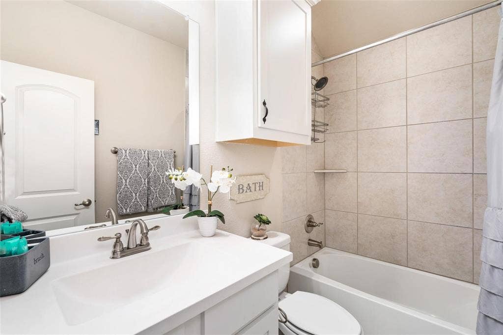 1017 Hoyt Drive, McKinney, TX 75071 Vanity with integrated sink, white cabinetry with dark hardware, full-width mirror, tile shower surround, and built-in tub