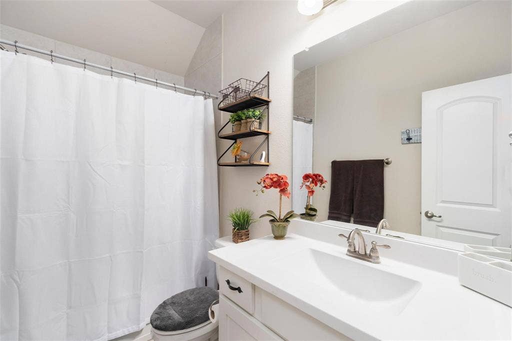 1017 Hoyt Drive, McKinney, TX 75071 White vanity with an integrated sink, brushed nickel faucet, wall-mounted mirror, and a shower with a privacy curtain