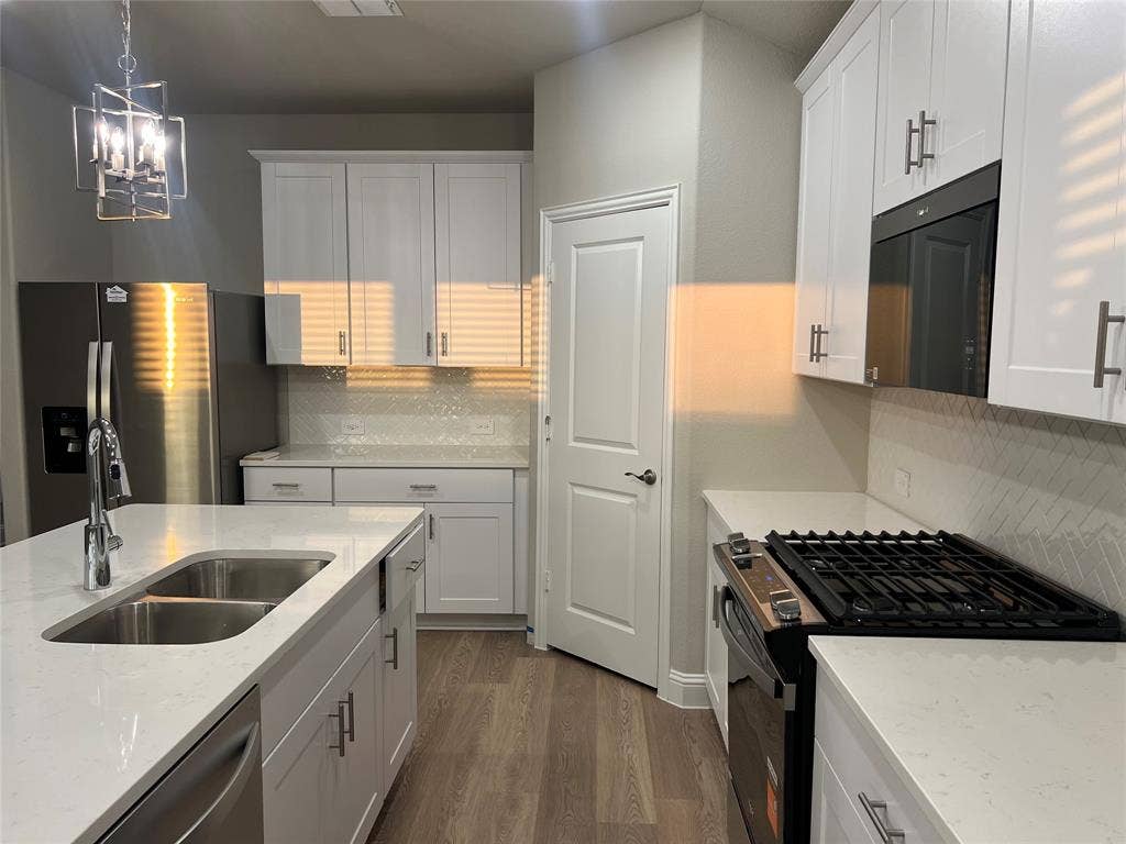 5908 Brittner Drive, Princeton, TX 75071 Modern kitchen featuring white cabinetry, light countertops, wood-finish flooring, a double basin sink, and a stainless steel appliance suite