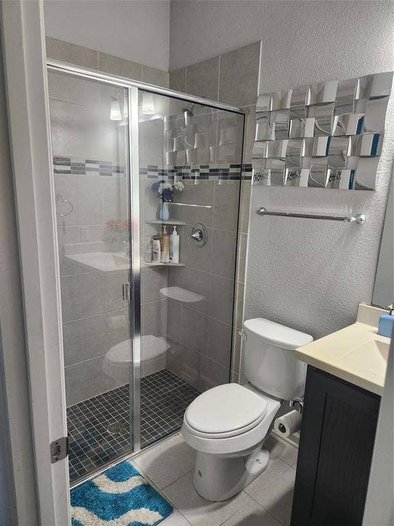 3038 Ivy Hill Lane, Irving, TX 75063 Shower enclosure with glass panels, light gray wall tile, dark gray mosaic shower floor, and an integrated shelf