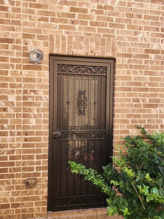 3038 Ivy Hill Lane, Irving, TX 75063 Exterior entryway featuring a masonry brick facade, decorative dark metal security door with intricate scrollwork, and a wall-mounted lantern-style exterior light fixture