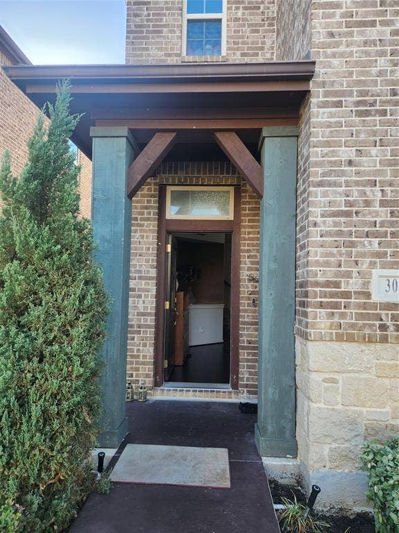 3038 Ivy Hill Lane, Irving, TX 75063 Brick exterior with stone accents, covered entryway with wood-finish beams, and transom window above the door