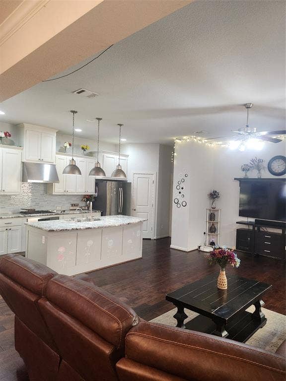 3038 Ivy Hill Lane, Irving, TX 75063 Open-concept living space with dark wood-finish flooring, white kitchen cabinetry, a kitchen island with pendant lighting, stainless steel appliances, and a ceiling fan