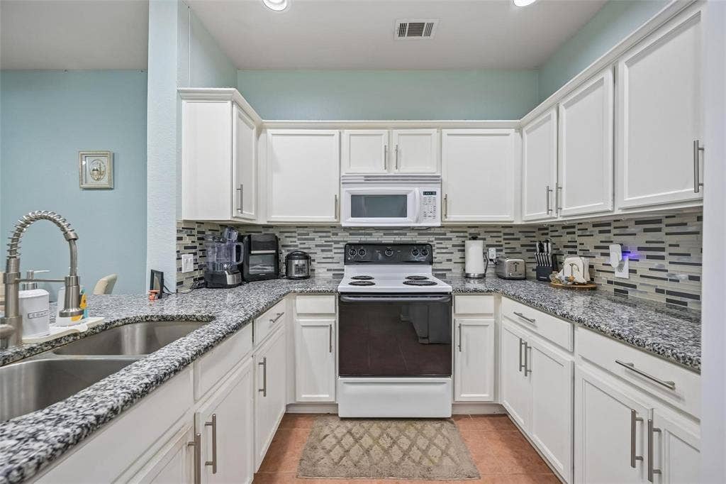 2209 Stonepark Place, McKinney, TX 75071 U-shaped kitchen featuring white cabinetry, stainless steel sink with pull-down faucet, mosaic tile backsplash, and dark speckled countertops