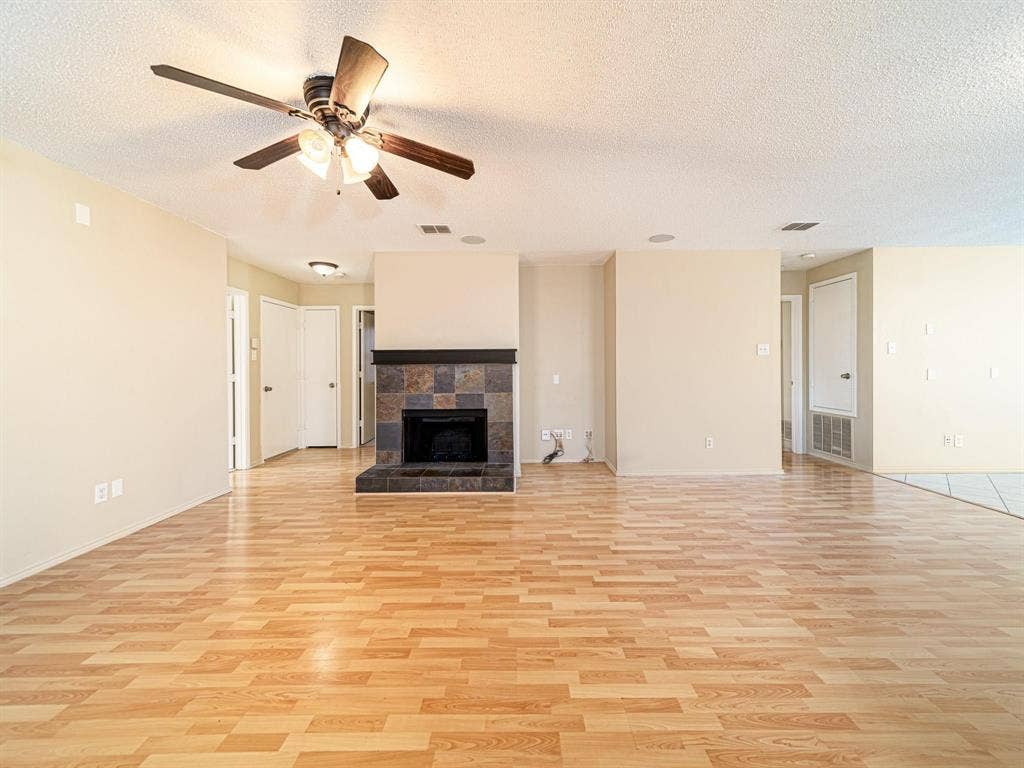 Spacious room featuring wood-finish flooring, a ceiling fan with integrated lighting, a fireplace with a stone surround, and recessed ceiling speakers