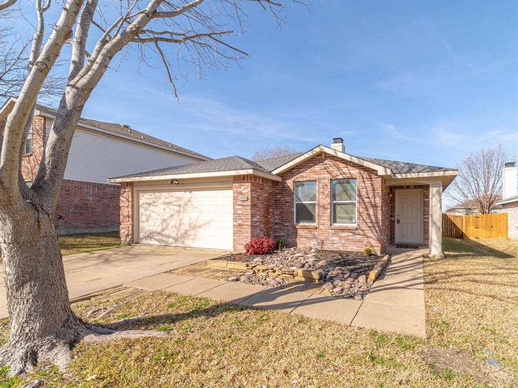 Brick exterior with an attached garage, covered entryway, and front landscaping with decorative rock