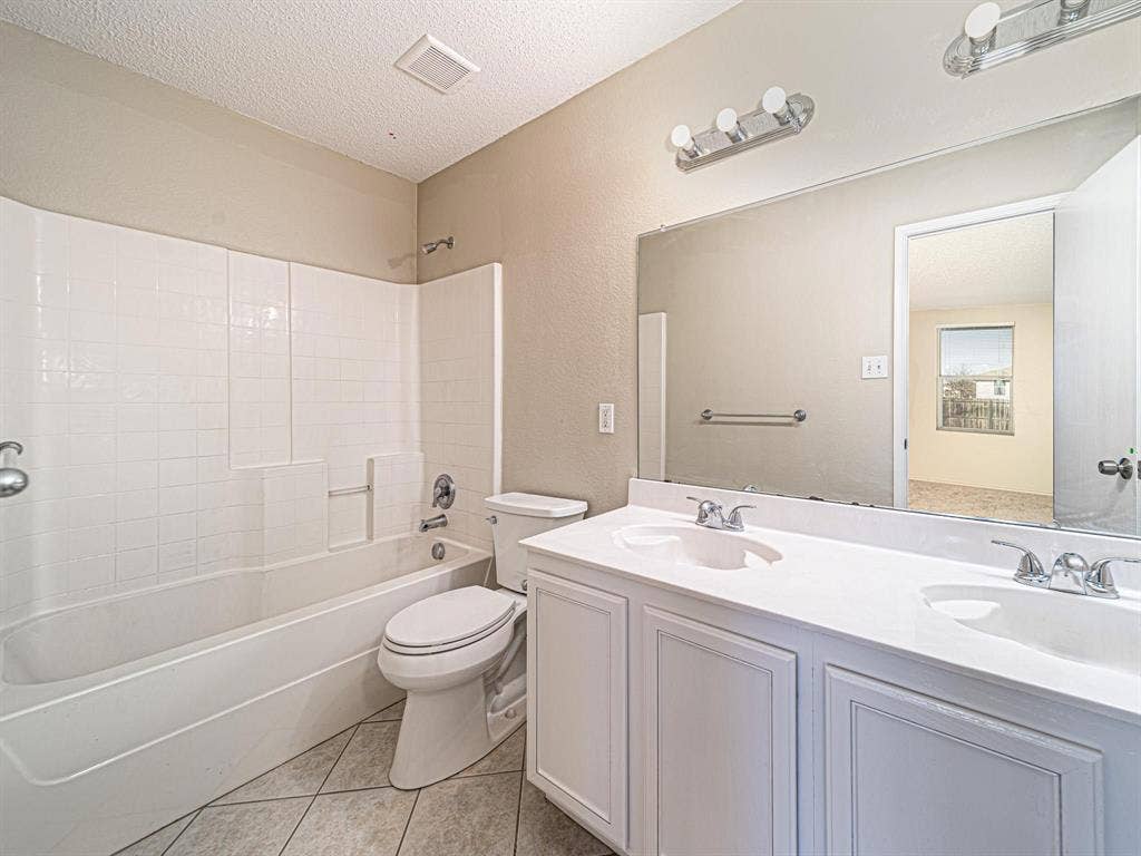 Bathroom featuring a dual vanity with integrated sinks, white cabinetry, a large mirror, a chrome-finish light fixture, and a tiled shower/tub combination