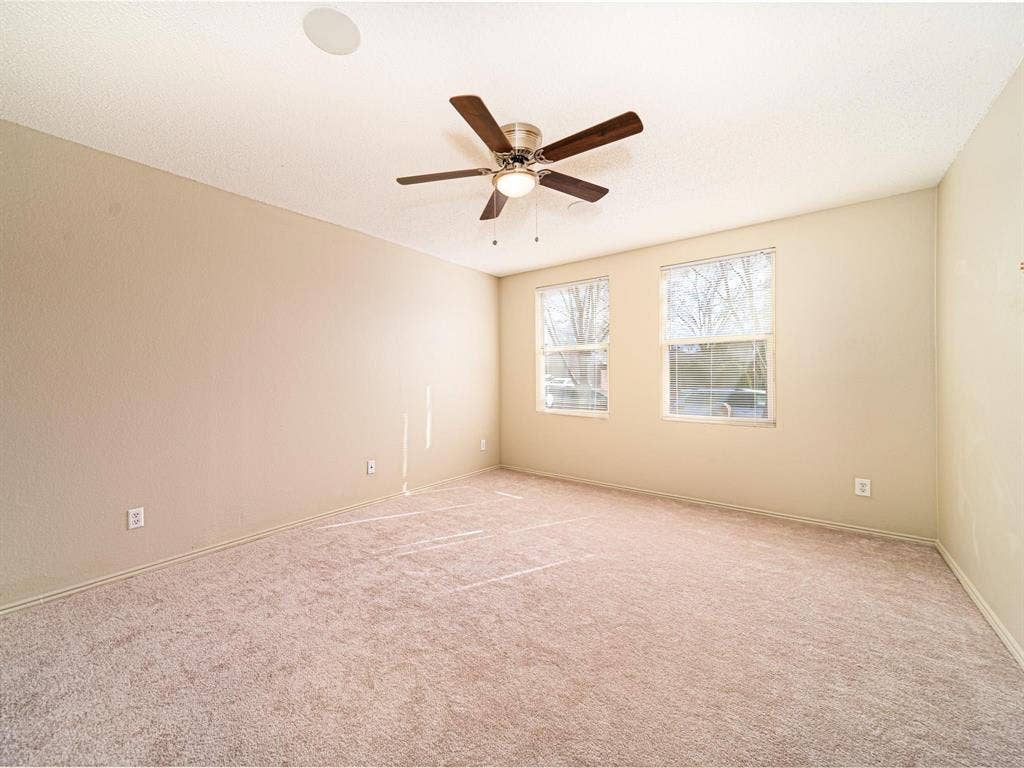 Neutral tone wall finishes, two windows with natural light, textured ceiling, ceiling fan with integrated lighting, and neutral tone carpeting