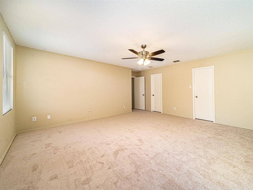 Spacious room featuring neutral carpeting, light-colored walls, and a ceiling fan with integrated lighting