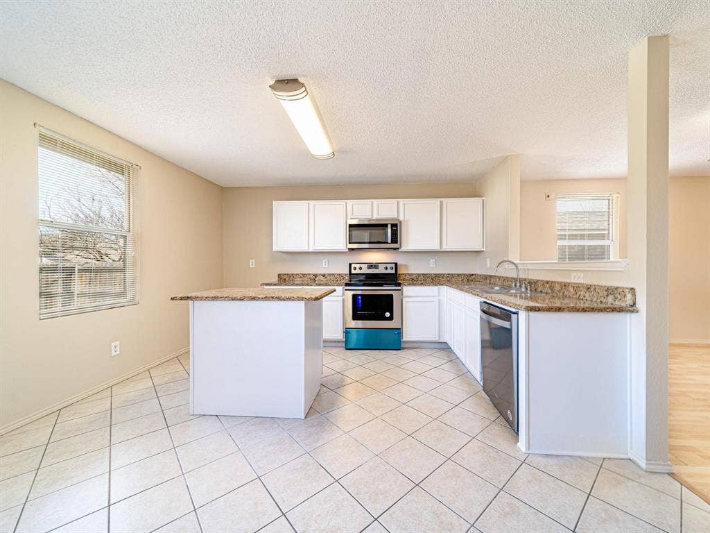 Kitchen featuring white cabinetry, granite-style countertops, stainless steel appliances, and a central island