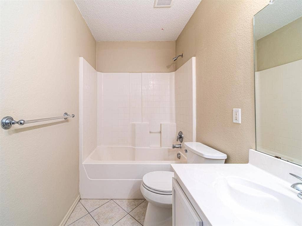 Tile flooring, bathtub with tile surround, white vanity, integrated sink, and wall mirror