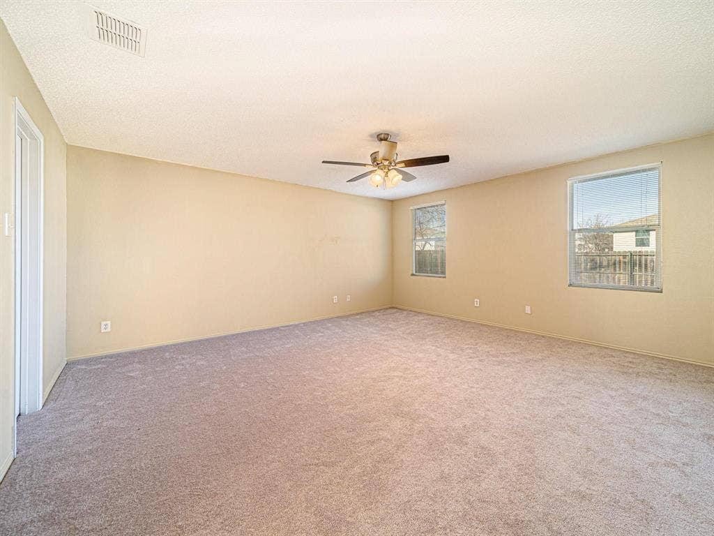 Expansive carpeted room featuring two windows and a ceiling fan with integrated lighting