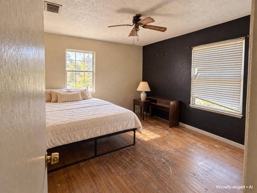 544 Pleasant Meadows Lane, Dallas, TX 75217 Bedroom featuring wood flooring, contrasting accent wall, ceiling fan, and two windows providing natural light. Virtually staged.