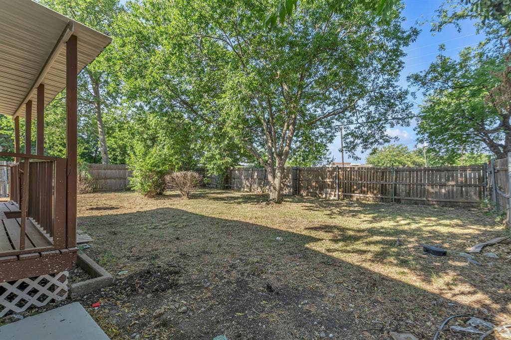 9621 Rustown Drive, Dallas, TX 75228 Expansive backyard featuring mature trees, partial wood fencing, and a covered porch with wood railing