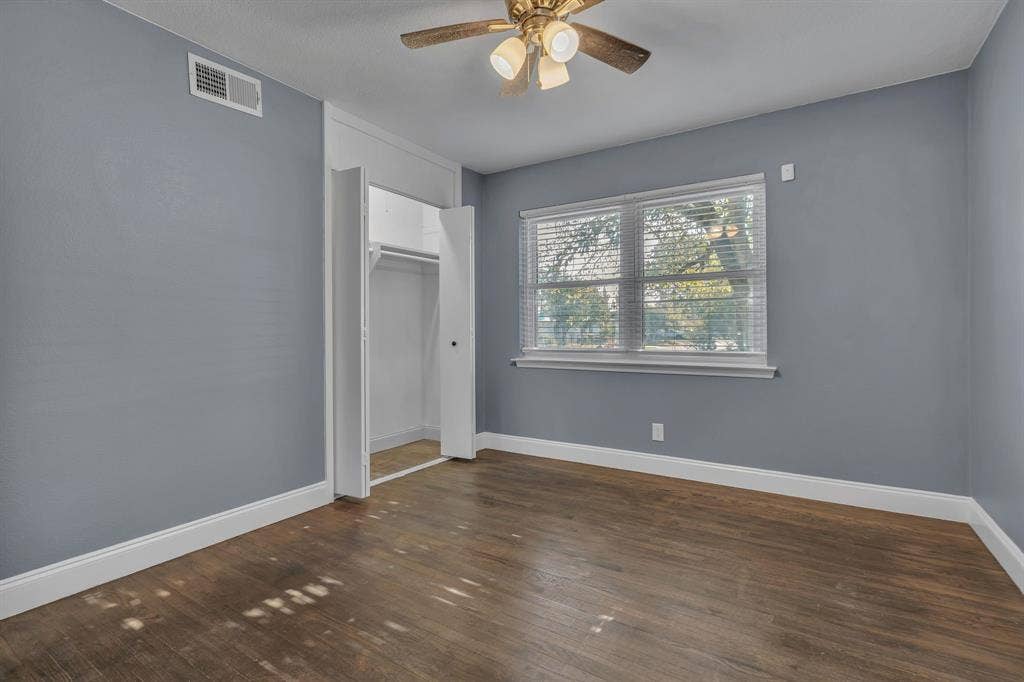 9621 Rustown Drive, Dallas, TX 75228 Wood-finish flooring, light blue wall paint, a ceiling fan with integrated lighting, a window with horizontal blinds, and a built-in closet with bi-fold doors