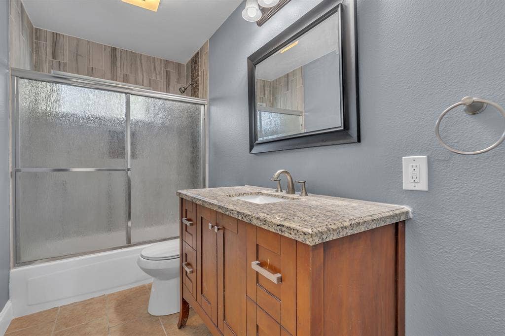 9621 Rustown Drive, Dallas, TX 75228 Wood-finish vanity with a stone countertop, an undermount sink, and a framed mirror