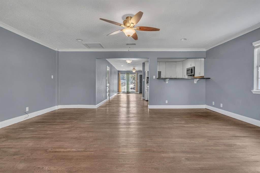Wood-finish flooring throughout, ceiling fan with integrated lighting, crown molding, and a pass-through counter to the kitchen featuring a built-in microwave