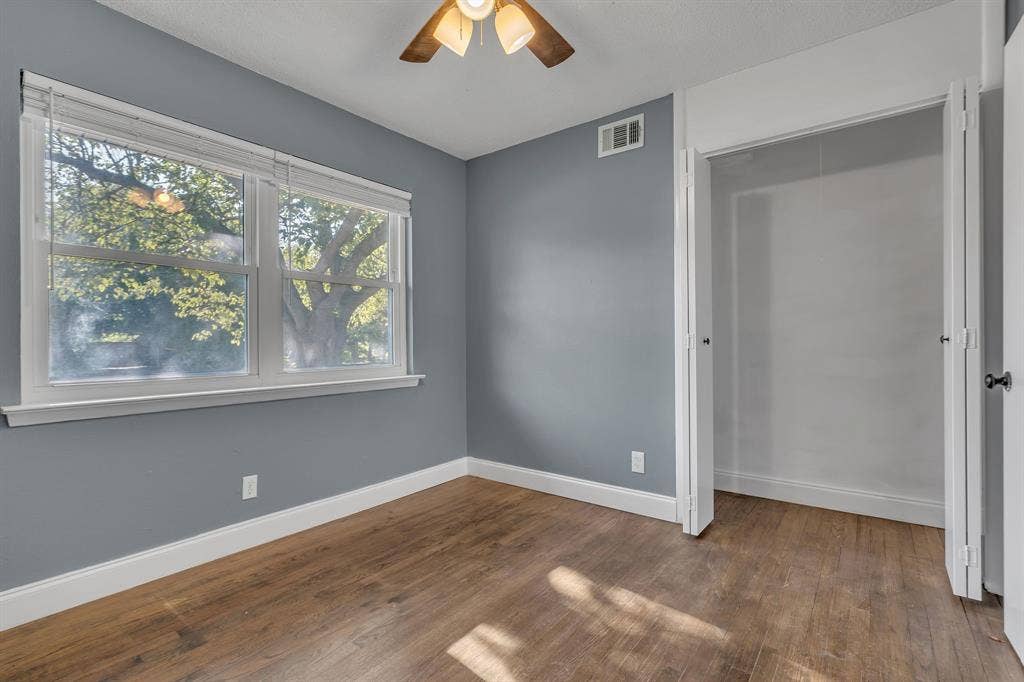 Wood-finish flooring with white trim, a large window with blinds, and an open closet