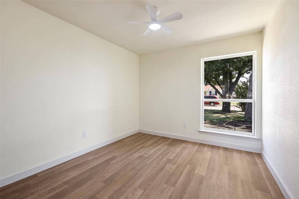 Wood-finish flooring, white walls, white trim, single window, and a ceiling fan with integrated lighting