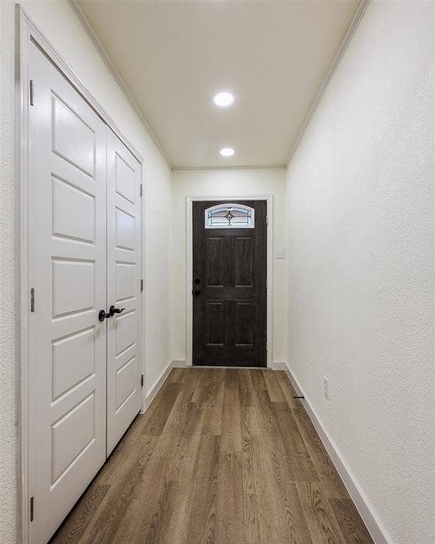 Wood-finish flooring leading to a dark wood entry door with decorative glass