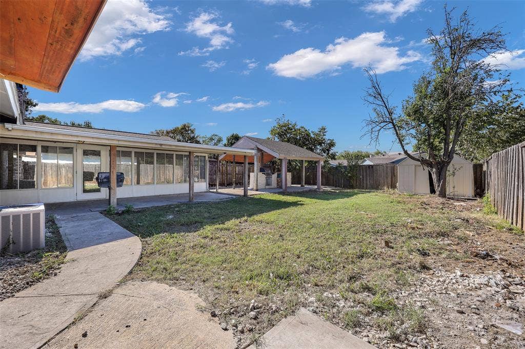 Expansive backyard featuring a concrete patio, covered outdoor structure, and a storage shed