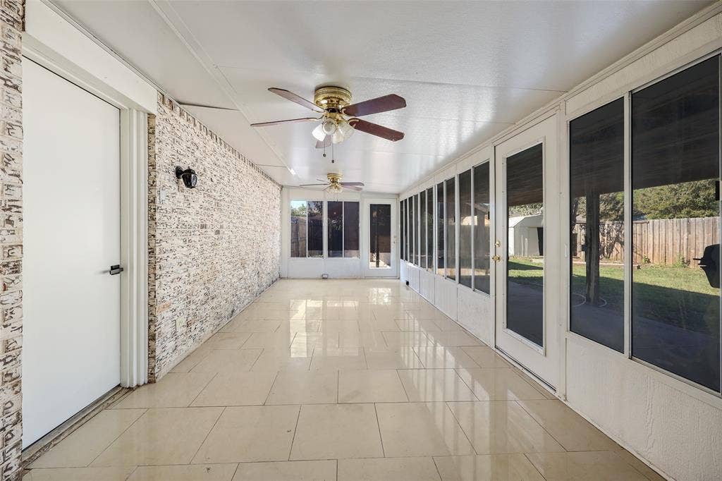 Enclosed sunroom featuring tile flooring, a textured brick-finish accent wall, ceiling fans, and multiple screened panels