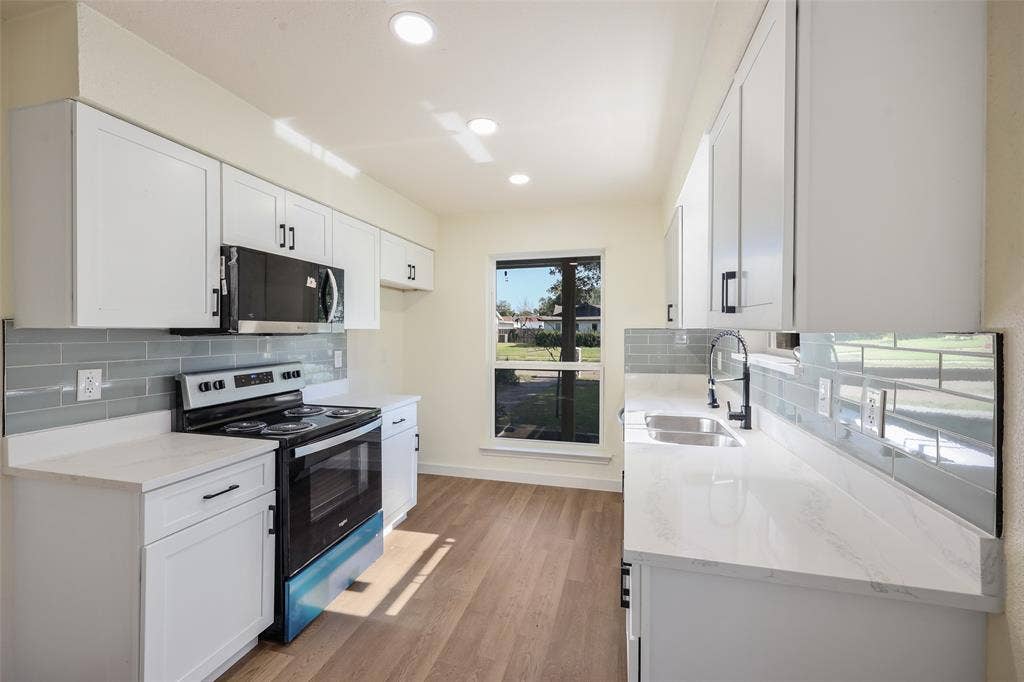 White cabinetry with black hardware, light-toned countertops, a full-size range, a dual-basin stainless steel sink with a matte black faucet, and wood-finish flooring