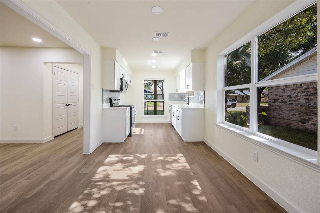 Spacious kitchen with wood-finish flooring, white cabinetry, built-in appliances, and recessed lighting