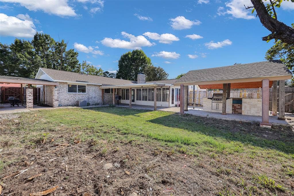 Brick exterior, covered outdoor kitchen with built-in grill, attached covered patio, sunroom, and mature trees
